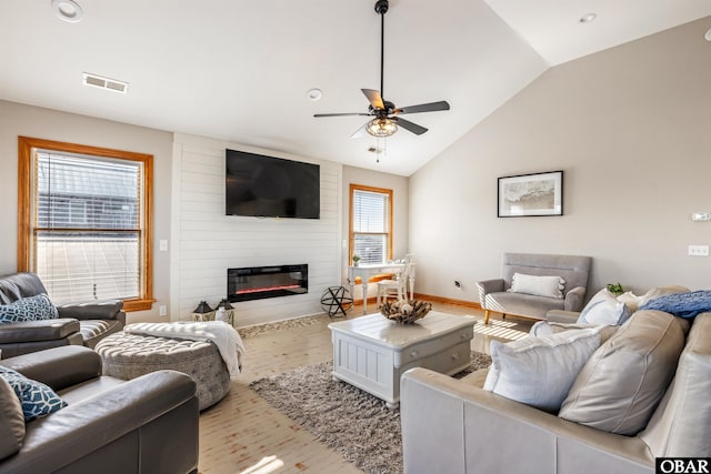 living area featuring light wood finished floors, lofted ceiling, visible vents, a ceiling fan, and a large fireplace