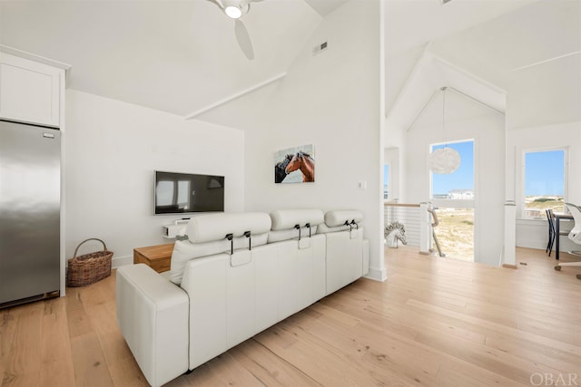 living room featuring light wood-style floors, visible vents, ceiling fan, and high vaulted ceiling