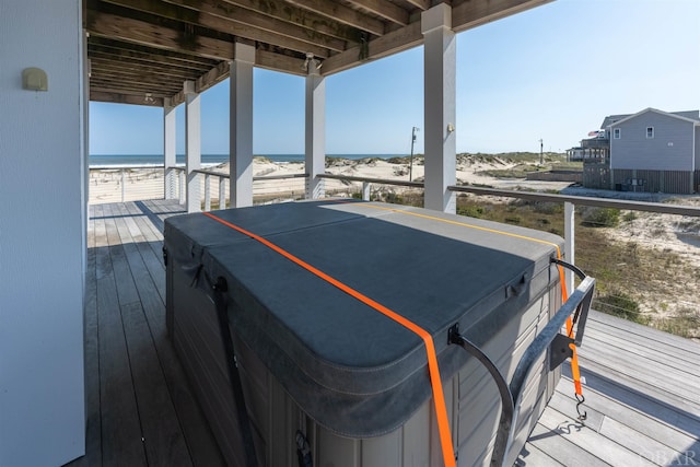 wooden deck with a water view, a beach view, and a hot tub