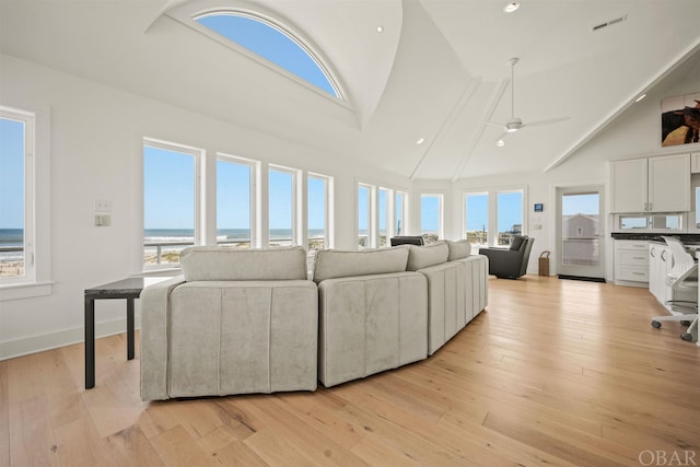 living room with light wood-style floors, a water view, ceiling fan, and high vaulted ceiling