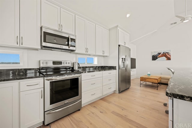 kitchen with light wood finished floors, stainless steel appliances, white cabinets, vaulted ceiling, and dark stone countertops