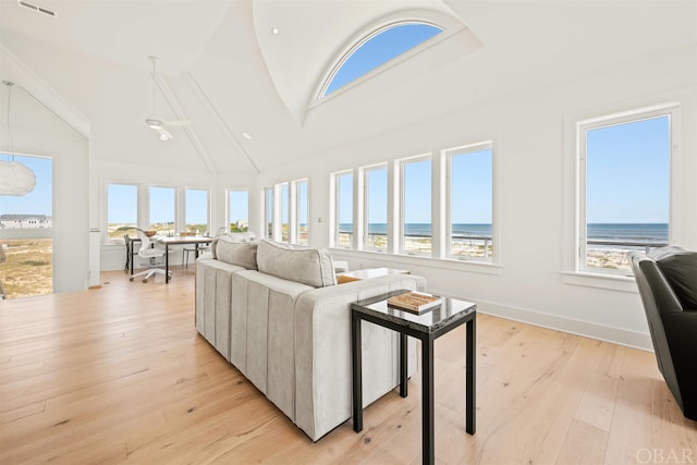 living room with a water view, light wood-style floors, baseboards, and high vaulted ceiling