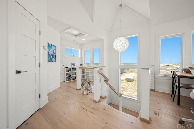 hall with light wood-style floors, attic access, baseboards, and an upstairs landing