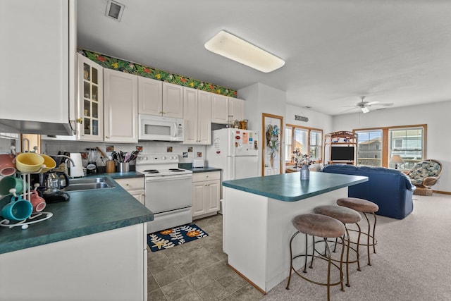 kitchen with dark countertops, white appliances, a kitchen breakfast bar, visible vents, and glass insert cabinets