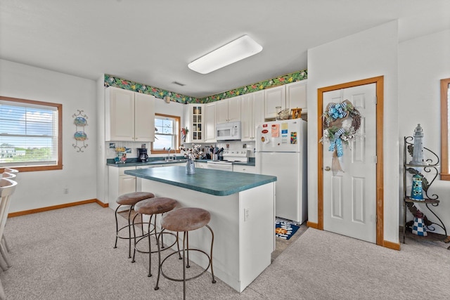 kitchen with dark countertops, light carpet, a sink, white appliances, and a kitchen bar