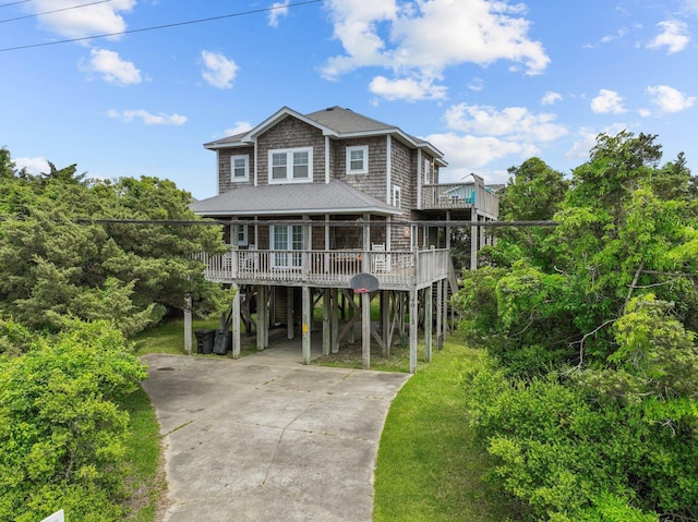 raised beach house featuring a wooden deck, a carport, a shingled roof, and concrete driveway