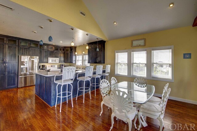kitchen with glass insert cabinets, dark brown cabinetry, a kitchen island, light stone countertops, and white appliances