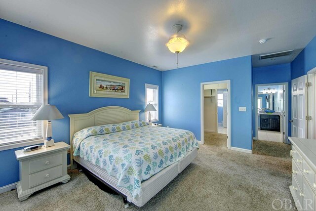 bedroom featuring light colored carpet, a ceiling fan, baseboards, visible vents, and ensuite bath