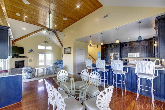 dining room with high vaulted ceiling, wooden ceiling, a fireplace, visible vents, and dark wood finished floors