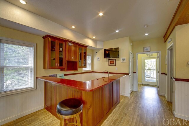 kitchen with light wood-style flooring, a breakfast bar area, glass insert cabinets, a peninsula, and recessed lighting