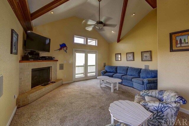 carpeted living room featuring high vaulted ceiling, beamed ceiling, a brick fireplace, and baseboards