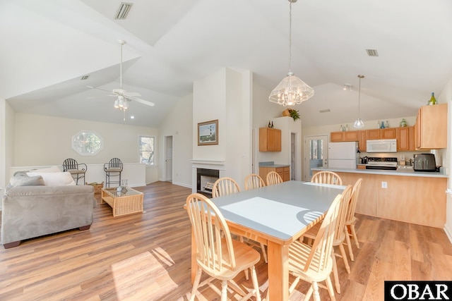 dining space featuring high vaulted ceiling, light wood-style flooring, a fireplace, and visible vents