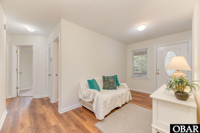 living area featuring light wood-type flooring, a textured ceiling, and baseboards