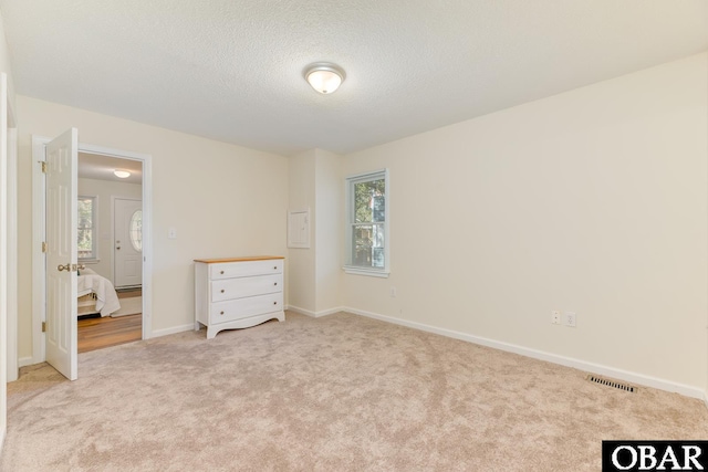 unfurnished bedroom featuring light carpet, baseboards, visible vents, and a textured ceiling