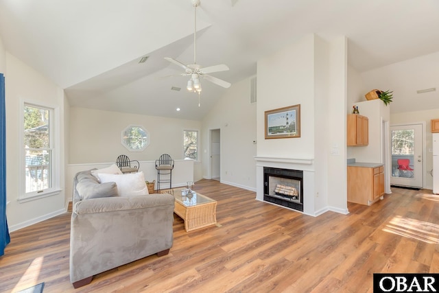 living area with a fireplace, visible vents, light wood-style flooring, high vaulted ceiling, and baseboards