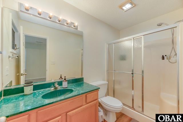 bathroom with toilet, a shower stall, a textured ceiling, and vanity