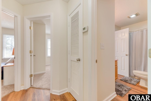 hall with light wood-type flooring, visible vents, and baseboards