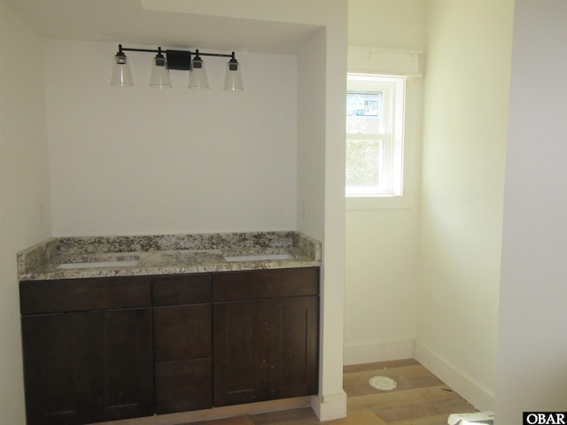 bathroom with baseboards, wood finished floors, and dual sinks