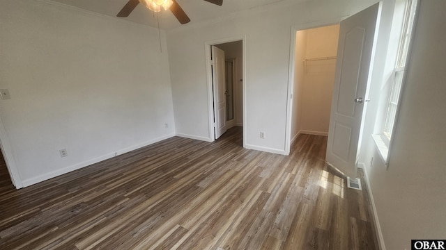 unfurnished bedroom featuring baseboards, dark wood-style floors, a closet, and a walk in closet