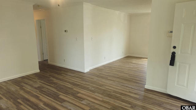 empty room with dark wood finished floors, crown molding, and baseboards