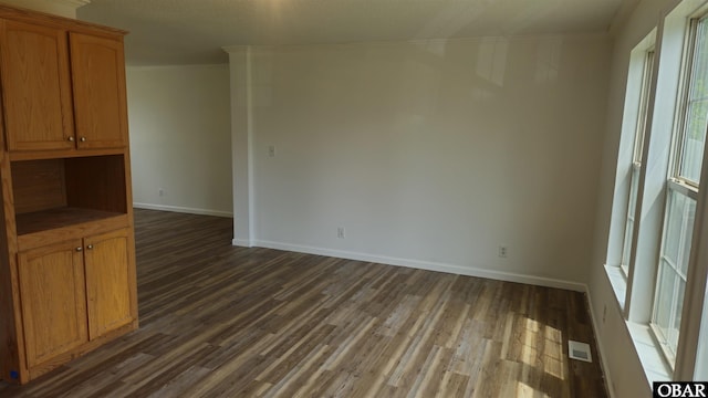 unfurnished room with dark wood-style floors, baseboards, ornamental molding, and visible vents