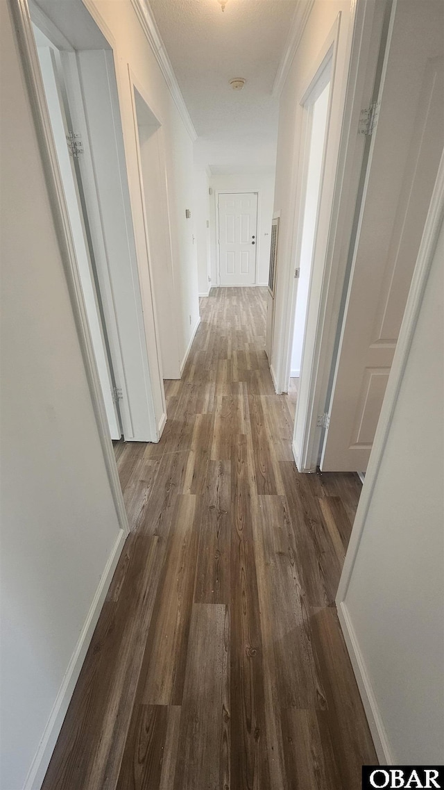 corridor featuring dark wood-type flooring, crown molding, and baseboards