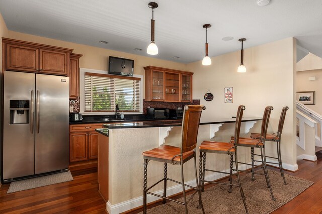 kitchen with brown cabinetry, stainless steel fridge with ice dispenser, dark countertops, dark wood-type flooring, and backsplash