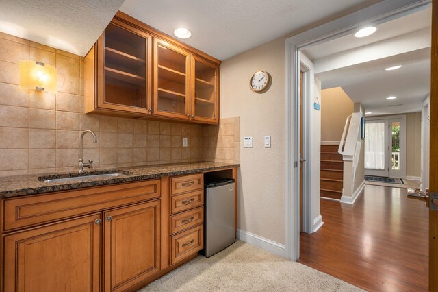 kitchen with decorative backsplash, glass insert cabinets, brown cabinets, dark stone countertops, and a sink