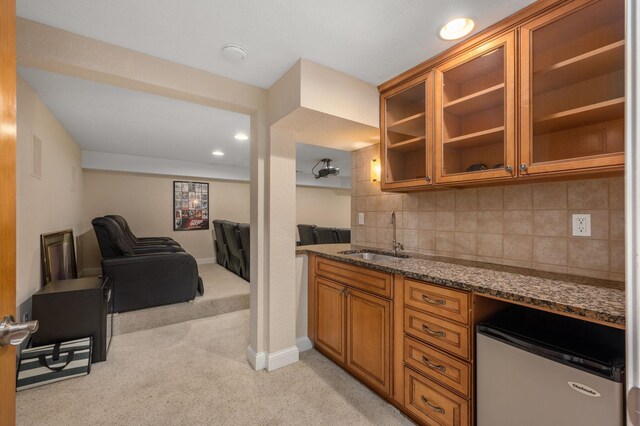 kitchen featuring light carpet, stone countertops, decorative backsplash, brown cabinets, and a sink