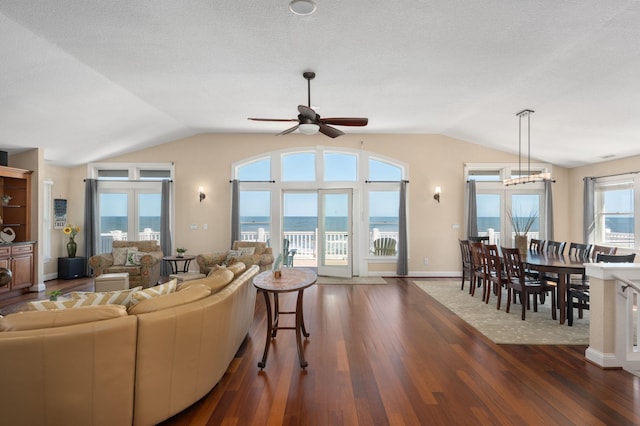 living area featuring baseboards, lofted ceiling, ceiling fan, dark wood-type flooring, and a water view