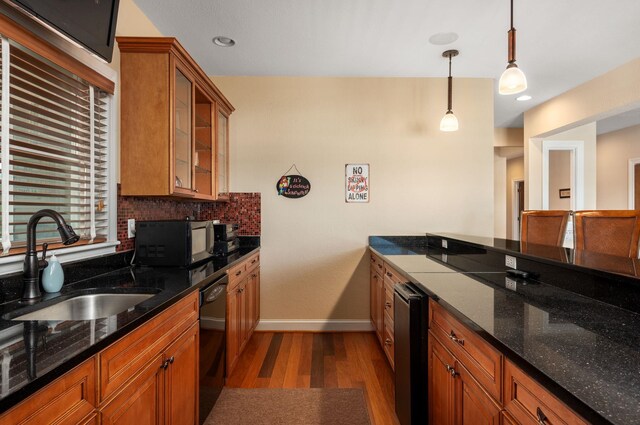 kitchen with wood finished floors, a sink, decorative backsplash, black appliances, and brown cabinetry