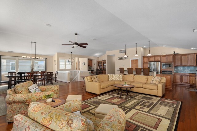 living room featuring dark wood finished floors, visible vents, vaulted ceiling, and ceiling fan with notable chandelier