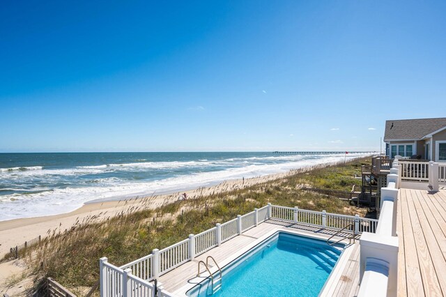 view of swimming pool with a fenced in pool, a deck with water view, and a beach view