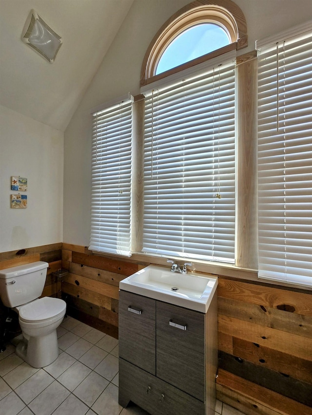 bathroom with toilet, wainscoting, vaulted ceiling, vanity, and tile patterned flooring