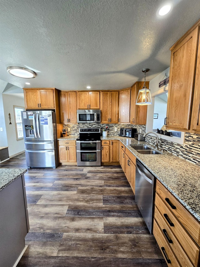 kitchen featuring stainless steel appliances, dark wood finished floors, decorative light fixtures, and a sink