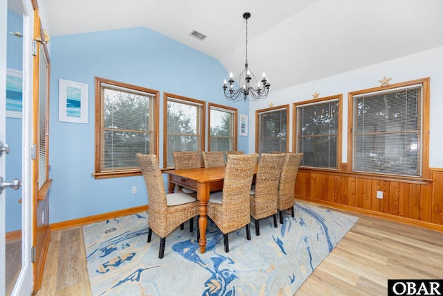 dining area featuring a chandelier, lofted ceiling, a wainscoted wall, wood walls, and light wood finished floors