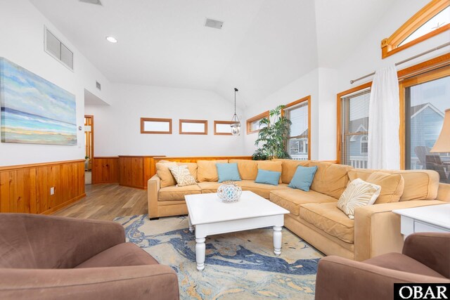 living room featuring wooden walls, visible vents, wainscoting, lofted ceiling, and light wood-style floors