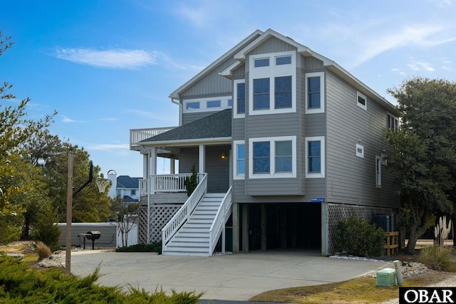 beach home with a shingled roof, covered porch, stairway, a garage, and driveway