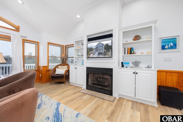 living area with a fireplace, light wood finished floors, lofted ceiling, wainscoting, and wood walls