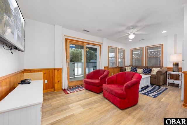 living room featuring a wainscoted wall, visible vents, light wood finished floors, and a ceiling fan