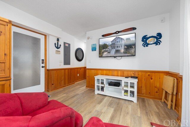 living area featuring a textured ceiling, a wainscoted wall, wood walls, light wood-type flooring, and electric panel