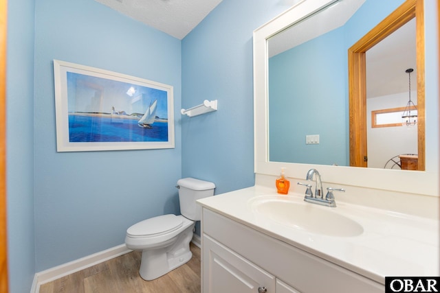 bathroom featuring toilet, baseboards, wood finished floors, and vanity