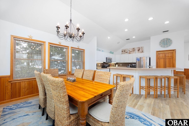 dining space featuring wooden walls, wainscoting, lofted ceiling, light wood-type flooring, and a notable chandelier