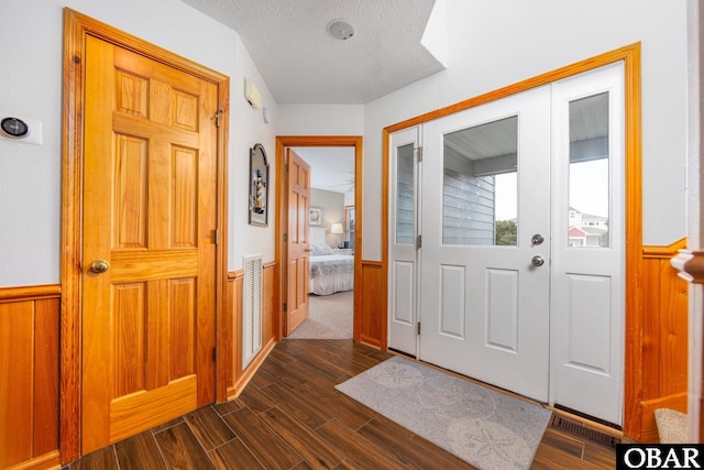 entrance foyer featuring dark wood-style flooring, a wainscoted wall, wood walls, and a textured ceiling