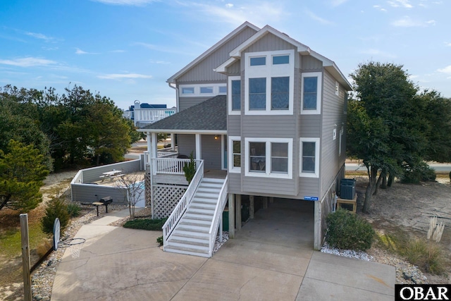 raised beach house featuring concrete driveway, stairs, central AC, a porch, and a carport