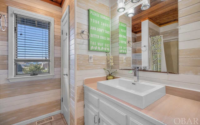 full bath with a shower with shower curtain, wooden walls, visible vents, and vanity