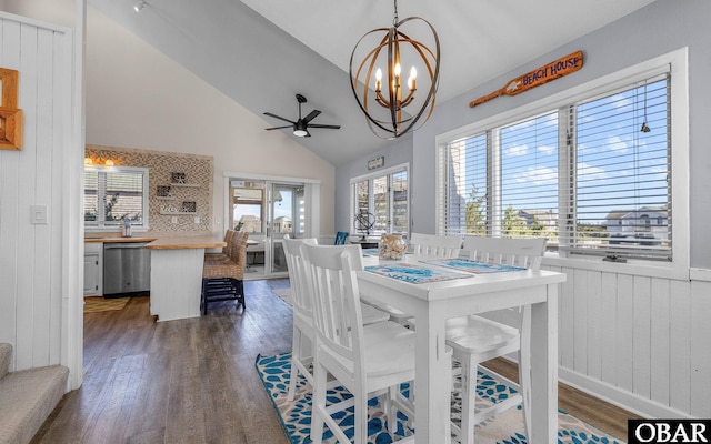 dining space with lofted ceiling, wooden walls, dark wood-type flooring, and ceiling fan with notable chandelier