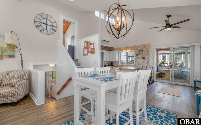 dining space featuring high vaulted ceiling, ceiling fan with notable chandelier, stairs, and wood finished floors