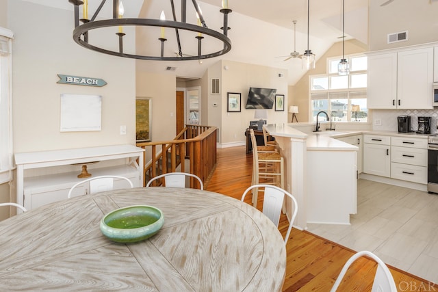 dining room featuring light wood-style floors, a ceiling fan, visible vents, and high vaulted ceiling