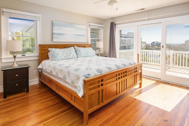 bedroom with a textured ceiling, light wood finished floors, visible vents, and access to exterior